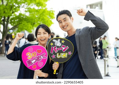 Asian couple who came to see a concert with cheering fans. Japanese translation: "shoot with bang!","stare for 3 seconds"