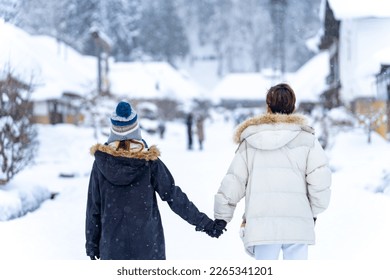 Asian couple in winter coat walking down street during travel at Ouchi-juku village in Fukushima prefecture in snow day. People tourist enjoy outdoor lifestyle travel Japan on winter holiday vacation. - Powered by Shutterstock