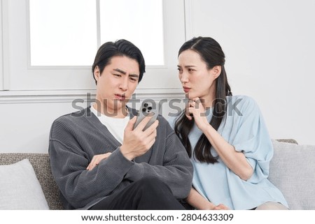 Asian couple worrying while looking at smartphone in living room