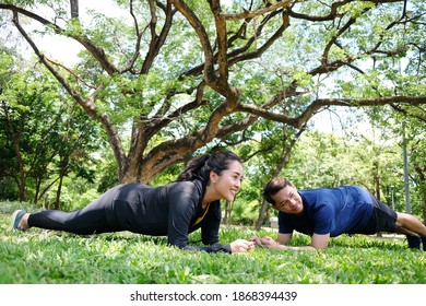 Asian Couples Exercising And Planking Workout Together On Grass Field In The Garden. Social Distancing And New Normal Life Concept