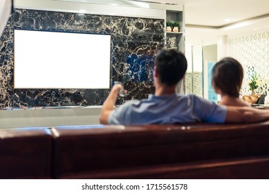 Asian couples watching white blank screen display television for advertising template background.  People lifestyles concept. Lockdown social distancing work from home. Selective focus on TV