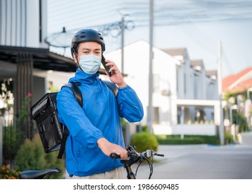 Asian courier man in uniform wear medical face mask, helmet using bicycle with backpack for food delivery of order to customer. Online order during quarantine and outbreak of coronavirus or covid 19. - Powered by Shutterstock