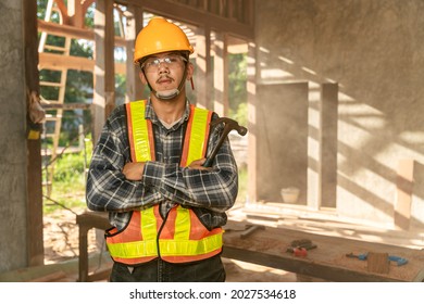 Asian Craftsman With Holding A Hammer In Hands Standing In Spacious Workshop And Looking At Camera On Construction Site