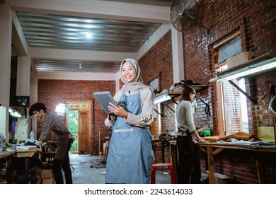 Asian craftswoman in veil smiling using digital tablet in studio - Powered by Shutterstock