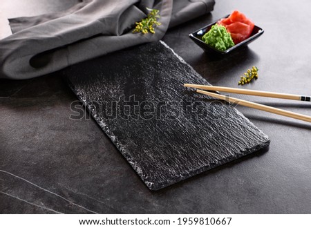 Asian cuisine - Black Slate Plate with Chopstick. Place setting with wasabi and pickle ginger. Empty sushi plate on black stone table