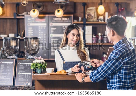 Asian customer man paying with credit card via contactless nfs technology to Asian Barista of Small business owner at the table in coffee shop, Small business owner and startup in coffee shop concept