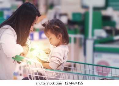 Asian Customer Mom And Her Baby With Shopping Cart Be Waiting At Cash Point In Supermarket And They Be Looking Something In Smartphone, Image Be Mobile Used For Await.