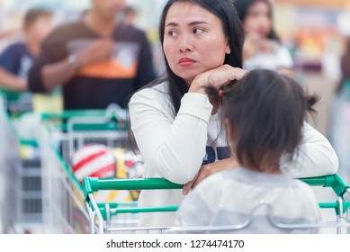 Asian Customer Mom And Her Baby With Shopping Cart Be Waiting At Cash Point In Supermarket, Emotional Of Bored With Long Time Await, Image Be Used Of Symbol Or Abstract Concept.