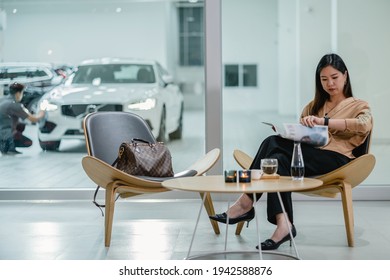 Asian Customer Woman Reading And Waiting Mechanic Checking For Maintain Her Car In Maintainance Service Center With The Part Of Showroom