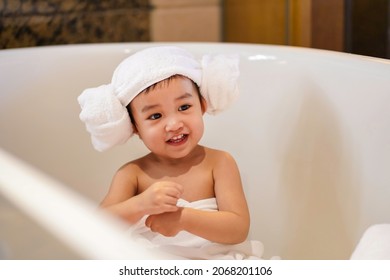 Asian Cute Baby Girl In A Bathrobe And Hair Wrapped In Towel Having Fun In A Bathtub