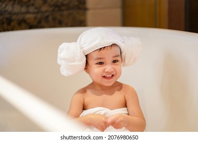 Asian Cute Baby Girl In A Bathrobe And Hair Wrapped In Towel Having Fun In A Bathtub