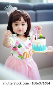 Asian cute baby girl celebrating with her first  birthday cake and number 1 candle on birthday party at home