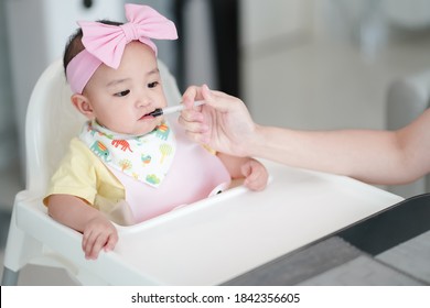 Asian Cute Baby Girl Taking A Liquid Drug After A Meal. Her Mother Is Injecting A Black Syrup Medicine, Iron In Syringe To Prevent Iron Deficiency Mostly Found In Baby