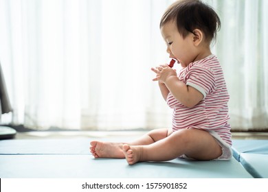 Asian Cute Baby Holding Toy And Trying To Eat It, Put Into Mouth, Sitting At Home. Dangerous Behavior Of Young Little Kid. If Things Not Clean Or Dirty, Reason Of Diarrhea Affection Sickness, Illness.