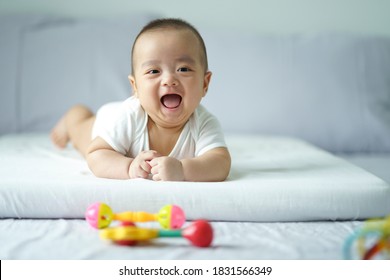 Asian Cute Baby In White Sunny Bedroom. Newborn Relaxing On Bed. Nursery For Young Children. Textile And Bedding For Kid. Family Morning At Home. New Born Kid During Tummy Time With Toy. Baby An