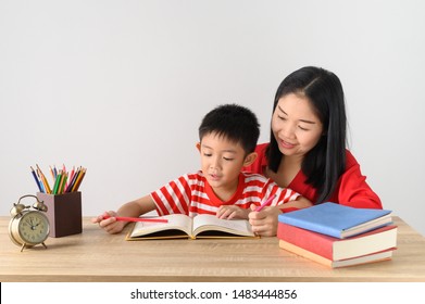 Asian Cute Boy Doing His School Homework With His Mother, At Home, He Is Writing On A Book.Education Concept