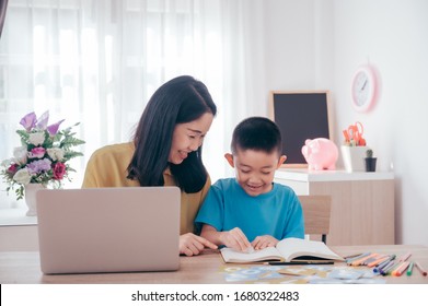 Asian cute boy doing his school homework and his mother use laptop at home, he is writing on a book.Education technology concept