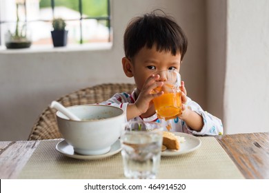 Asian Cute Boy With Pajama Drink Orange Juice And Eat Breakfast, Bread And Rice Soup