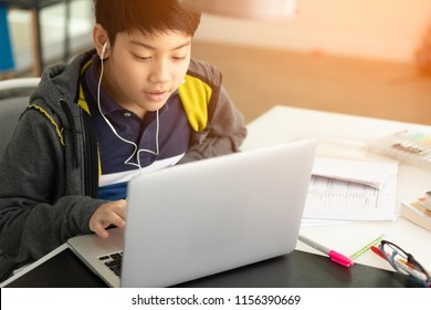 Asian cute boy using laptop computer with sunlight in the morning at home.