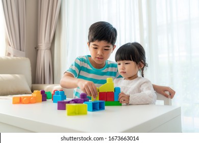 Asian cute brother and sister play with a toy block designer on the table in living room at home. Concept of bonding of sibling, friendship and learn through play activity for kid development.