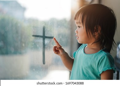 Asian cute child drawing cross on the window, Stay at home in quarantine. Covid-19 new normal concept, Coronavirus and Air pollution pm2.5 concept, spirituality and religion.