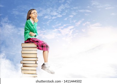 Asian cute girl with glasses think while sitting on the pile of books with blue sky background. Back to School concept - Shutterstock ID 1411444502