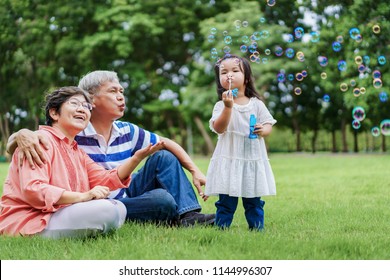 Asian cute granddaughter making bubbles and attractive happy grandparents look at her in the public garden at vacation day or holiday. Family Concept. - Powered by Shutterstock