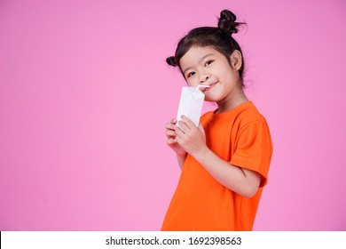 Asian Cute Kid Girl Drinking Milk Or Yogurt From Paper Box Isolated On Pink Background