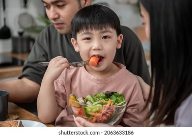 Asiatischer Cute kleiner Junge, der Gemüsesalat mit seinen Eltern in der Küche isst. Sehr schöne asiatische Familie, die zusammen frühstückt. Herzlichen Glückwunsch zum Familienleben.
