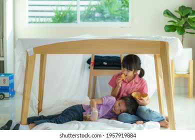 Asian Cute Little Boy Feeding Snack To His Sister Sibling While Sitting In A Blanket Fort In Living Room At Home For Perfect Hideout Away From Their Other Family 