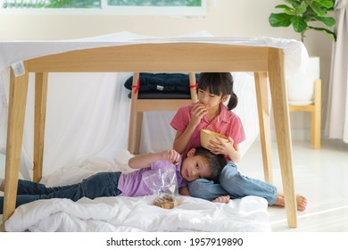 Asian Cute Little Boy Feeding Snack To His Sister Sibling While Sitting In A Blanket Fort In Living Room At Home For Perfect Hideout Away From Their Other Family 