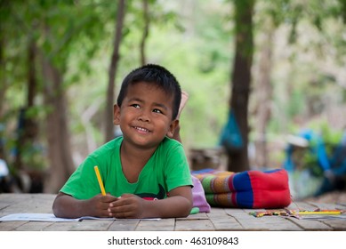 Asian Cute Little Boy(poor Kids) Is Drawing,painting With Color Pencil And Study At Old Home.Homeless Poor Children,smile,lying On Dirty Wooden Table And Writing Or Coloring Picture On Books.