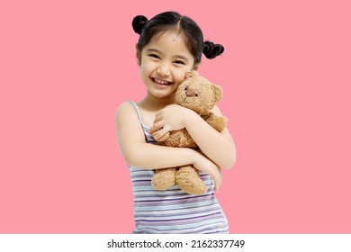Asian cute little Asian child girl hugging teddy bear isolated on pink background.