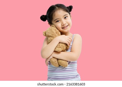 Asian Cute Little Asian Child Girl Hugging Teddy Bear Isolated On Pink Background.