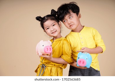 Asian Cute Little Couple Kid With Lovely Expression And Holding Pinky Piggy Bank