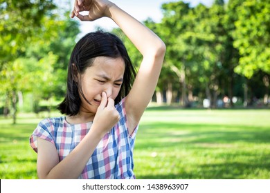 Asian cute little girl feel bad foul odor situation,smelling,sniffing her wet armpit in outdoor park,child feeling smell of sweat,problems due to hormonal changes,motion facial expression reaction