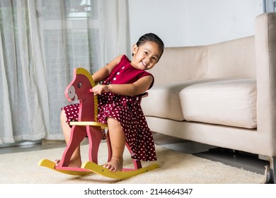 Asian cute little girl swinging riding toy horse, Smiling kid playing horse rocking chair at home in living room, Happy time to play during self kindergarten preschool