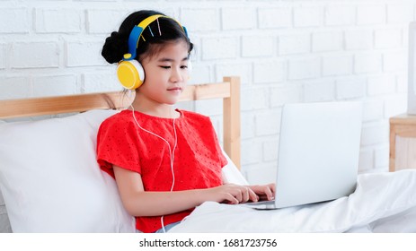 Asian Cute little girl wear headphones to learn online using a laptop. Is a Homeschool. Studying in the bedroom with a good environment. And Corinavirus Prevention (COVID-19). Concept education - Powered by Shutterstock