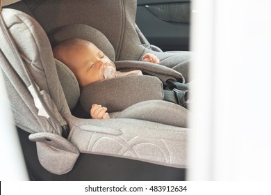 Asian Cute Newborn Baby Sleeping In Modern Car Seat. Child New Born Traveling Safety On The Road. Safe Way To Travel Fastened Seat Belts In A Vehicle With Young Kids. Trip With An Infant.