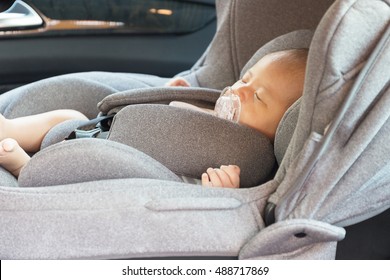 Asian Cute Newborn Baby Sleeping In Modern Car Seat. Child New Born Traveling Safety On The Road. Safe Way To Travel Fastened Seat Belts In A Vehicle With Young Kids. Trip With An Infant.