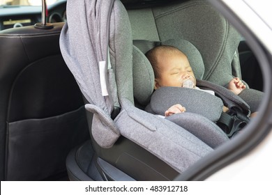 Asian Cute One Month Old Newborn Baby Sleeping In Modern Car Seat. Child New Born Traveling Safety On The Road. Safe Way To Travel Fastened Seat Belts In A Vehicle With Young Kids.