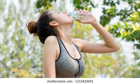 Asian cute sport healthy fit and firm slim teen girl drink water from plastic bottle on the hand in summer hot day at outdoor garden