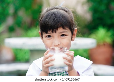 Asian cute student girl drinking a glass of milk at home before going to school in the morning. The concept is healthy and intelligent kid concept.    