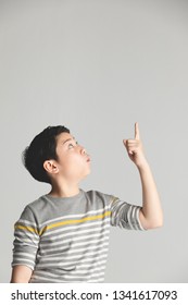 Asian Cute Teenager Boy In Gray Sweater Teenage Boy Points Up Over Gray Background, Half Body With Copy Space .