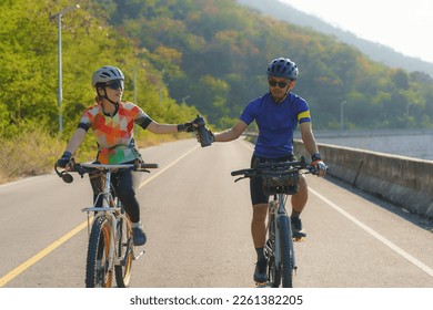 Asian cyclist man handing water bottle to his female cyclist girlfriend to drink water. While doing exercise together in the morning by the lake. - Powered by Shutterstock