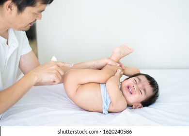 Asian Dad Is Applying Topical Cream To The Baby Boy For Skin Care On The Bed To Against Diaper Rash And Help The Baby Relief Itching Symptom.