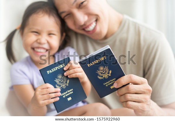 Asian dad and daughter holding amercian\
passports with pride. Immigration\
citizenship