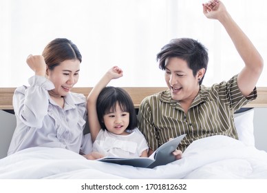 Asian Dad And Mom Are Reading Bedtime Stories To Their Daughter Before Sleeping