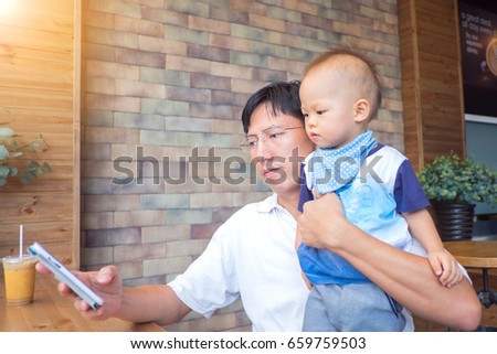 Asian Dad and son sitting in a cafe look in the phone, Father holding Cute little Asian 1 year old toddler baby boy child, leisure & technology & internet addiction concept / Selective focus at Dad
