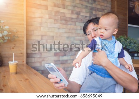 Asian Dad and son sitting in a city cafe look in the phone, Father holding Cute little Asian 1 year old toddler baby boy child at the restaurant, leisure & technology & internet addiction concept